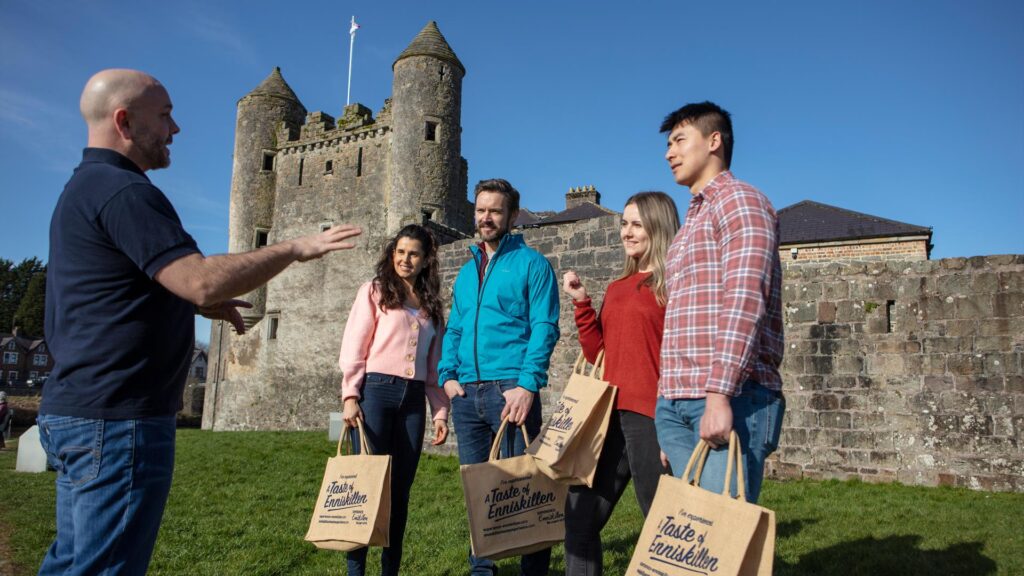 Group enjoying the Enniskillen Taste Experience tour outside Enniskillen Castle with local guide and shopping bags