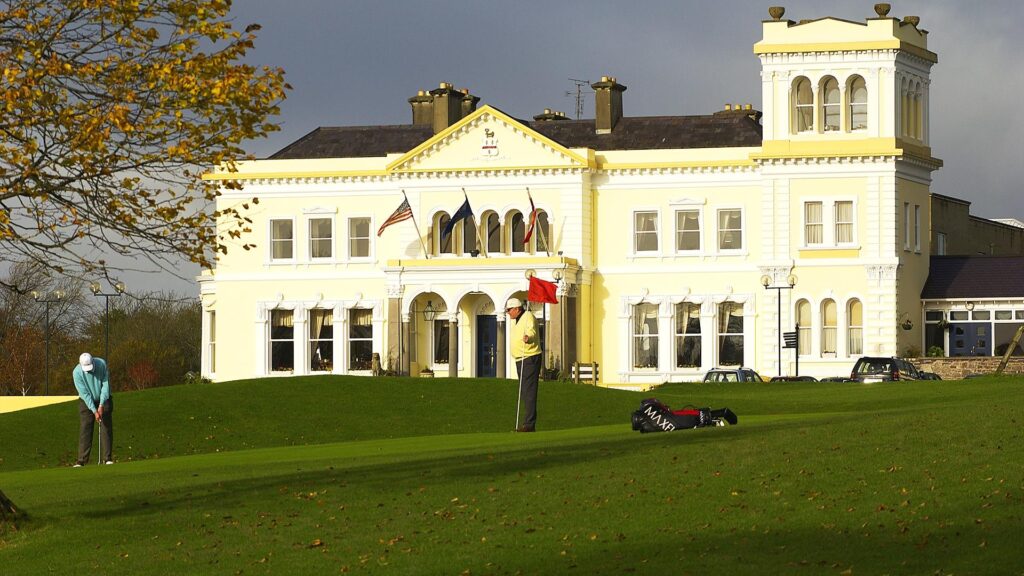 Golfers playing on the green in front of the historic Manor House Golf Course clubhouse in Enniskillen