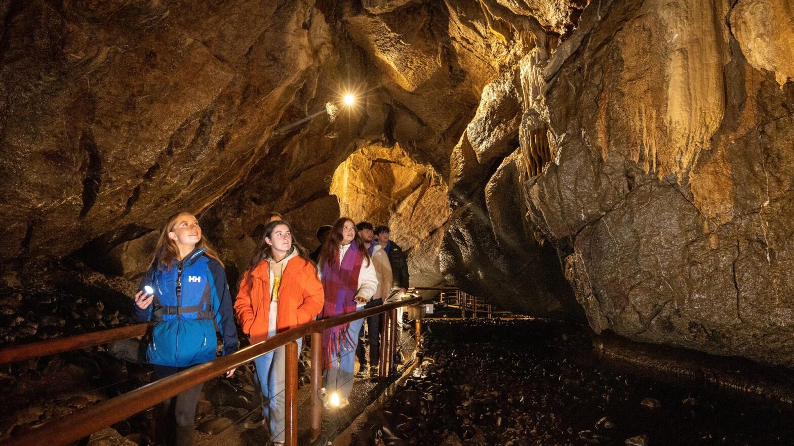 Tour group of people walk along a lit path inside a large marble arch cave with rocky walls and formations, enjoying an unforgettable corporate retreat near Enniskillen.