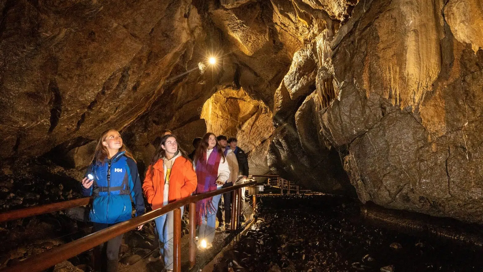 Tour group of people walk along a lit path inside a large marble arch cave with rocky walls and formations, enjoying an unforgettable corporate retreat near Enniskillen.