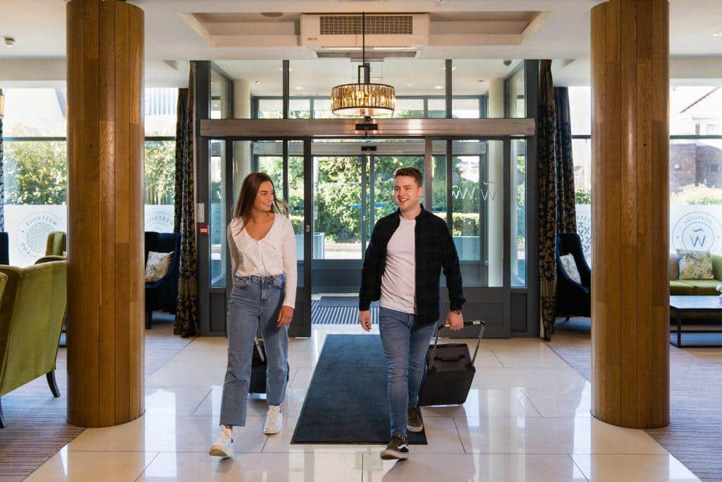 Two guests walking through the accessible entrance lobby at The Westville Hotel with luggage. Westville Hotel Enniskillen