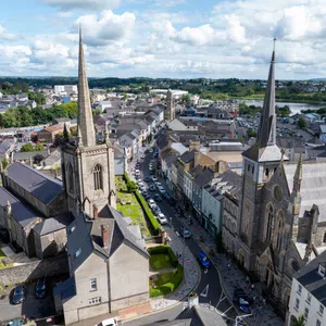 Aerial view of a town with historic stone churches featuring tall spires, rows of buildings, and a winding street with cars—Enniskillen Dining spots dot the scene under a partly cloudy sky. what to do in Enniskillen - unusual things to do in Enniskillen